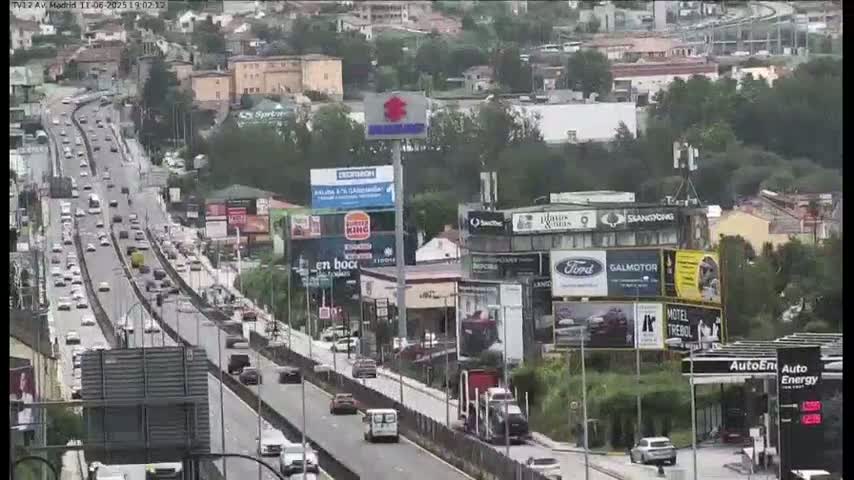 A highway scene on an overcast day shows a multi-lane road with moderate traffic, flanked by buildings with numerous billboards and advertising signs.
