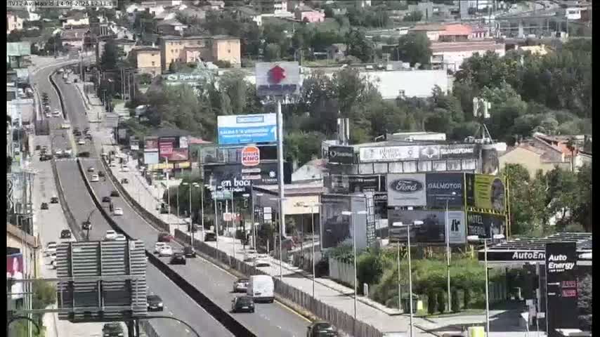 A highway with moderate traffic flows through a city on a sunny day, past buildings with numerous billboards and advertisements.
