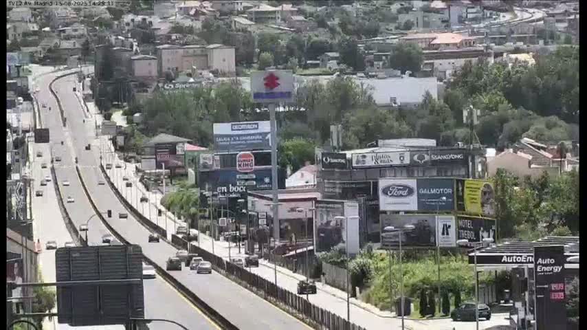 A multi-lane highway with moderate traffic flows through a city with numerous billboards and buildings on a partly sunny day.