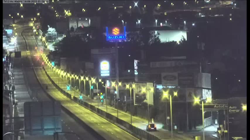A multi-lane highway with moderate traffic flows through a city with numerous billboards and buildings on a partly sunny day.