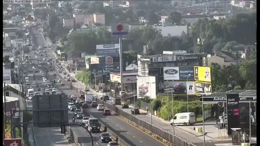 A hazy, sunny day shows a multi-lane highway with heavy traffic flowing through a city with numerous billboards and buildings.