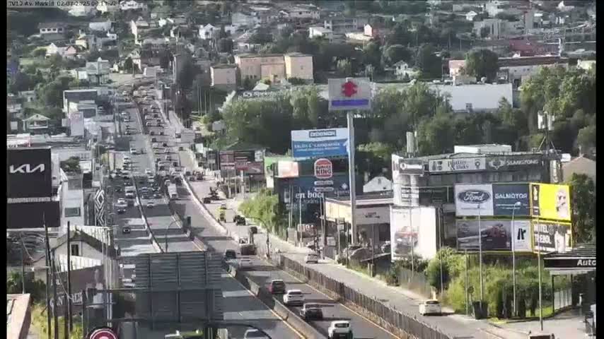 A multi-lane highway with moderate traffic flows through a city on a partly sunny day.