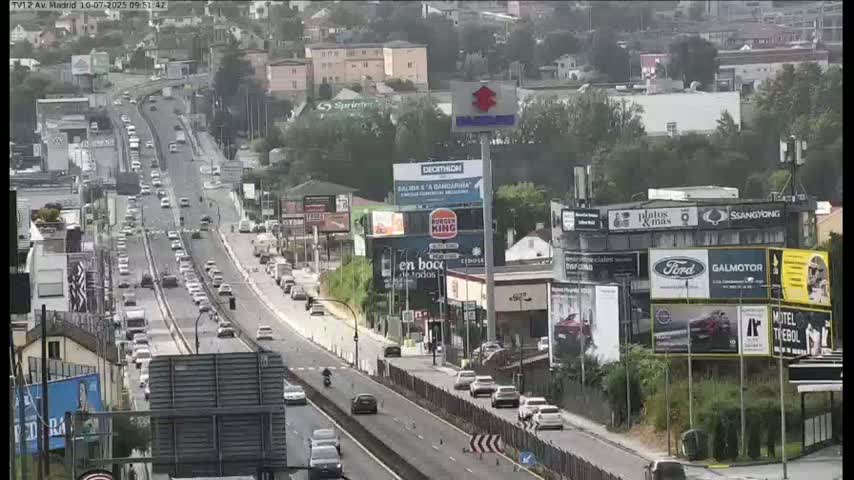 A multi-lane highway with moderate traffic flows through a cityscape on a partly cloudy day.