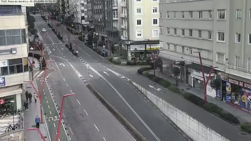 A mostly empty city street scene on an overcast day shows multi-story buildings lining either side of a two-lane road with bike lanes, a few pedestrians, and sparse vehicle traffic.