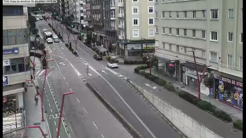 A mostly empty city street with a few cars and pedestrians is seen from an elevated vantage point on an overcast day.