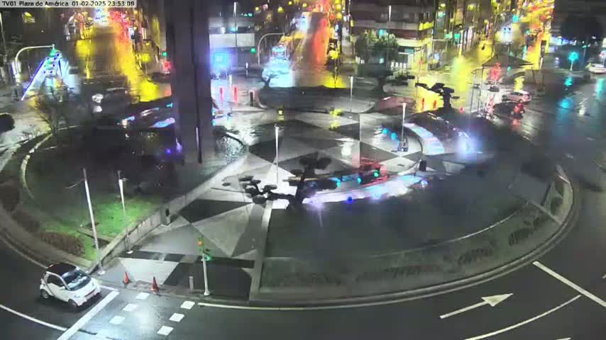 A nighttime, rain-slicked roundabout with a central fountain and several vehicles, surrounded by buildings and streetlights.