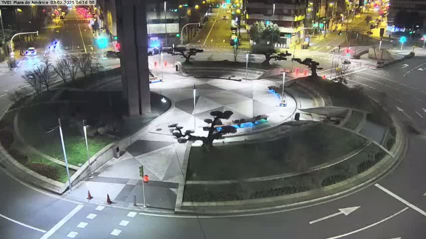 A nighttime aerial view of a roundabout with landscaped center islands and surrounding roadways, illuminated by streetlights.