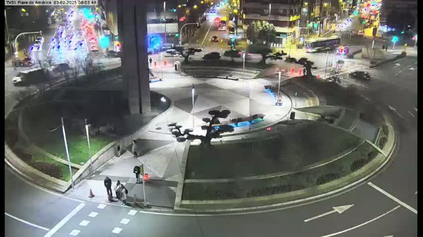 A nighttime aerial view of a circular plaza with a geometric design, surrounded by roads with cars and pedestrians, under clear night sky.