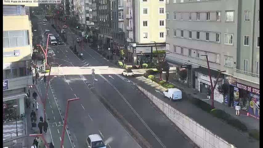 A sunny day on a city street shows several cars driving on a multi-lane road that has a bike lane, pedestrians walking on the sidewalk and buildings lining both sides of the street.