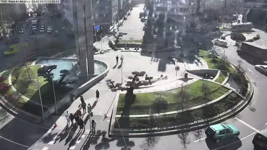 A sunny day view of a circular plaza with landscaping, pedestrians, and cars driving around the roundabout.