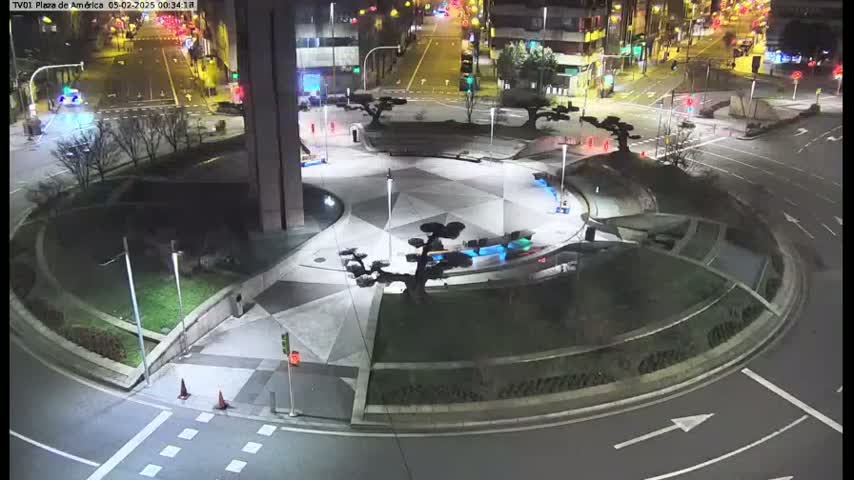 A nighttime, overhead view of a plaza with geometric landscaping, trees, and a circular roadway surrounding it.