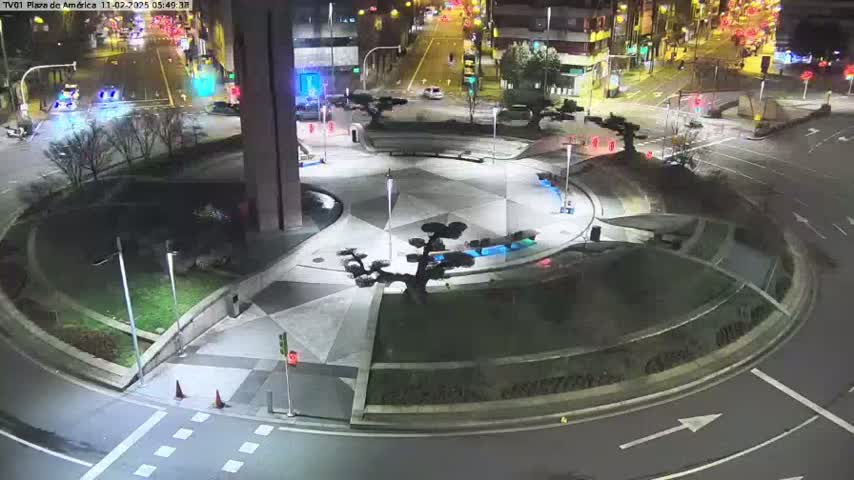 A nighttime aerial view of a circular plaza with landscaping features and surrounding roads, lit by streetlights.