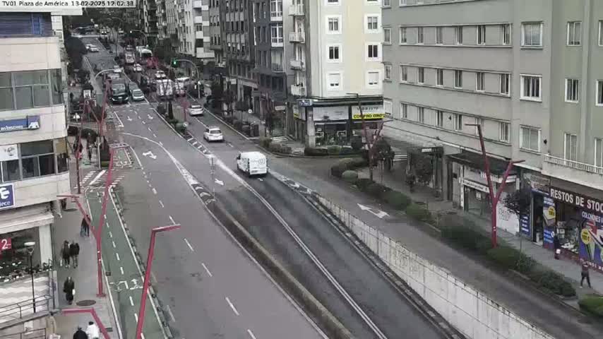 A mostly empty city street with light traffic, bordered by buildings and a bike lane, on an overcast day.