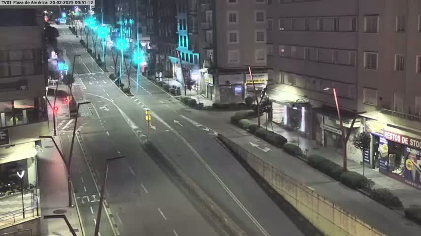 A mostly empty, multi-lane road at night is flanked by buildings, with streetlights illuminating the scene.