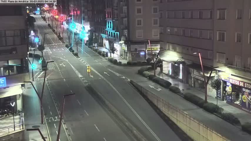 A mostly empty, four-lane road at night, lined with buildings and streetlights, under clear skies.