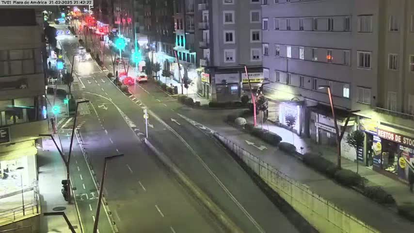 A nighttime, mostly empty street scene shows several vehicles on a multi-lane road that passes by buildings with street lights illuminating the area.