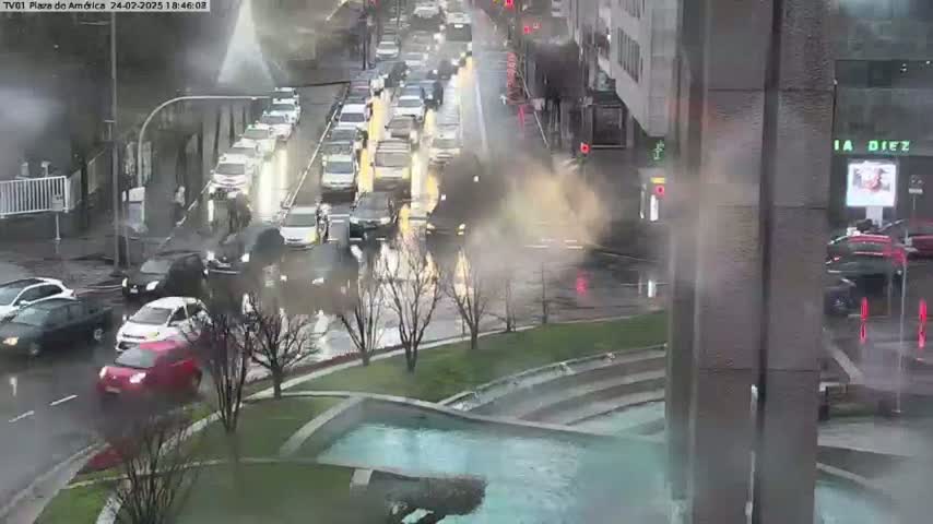 A rainy city street scene shows congested traffic and a water feature in the foreground.