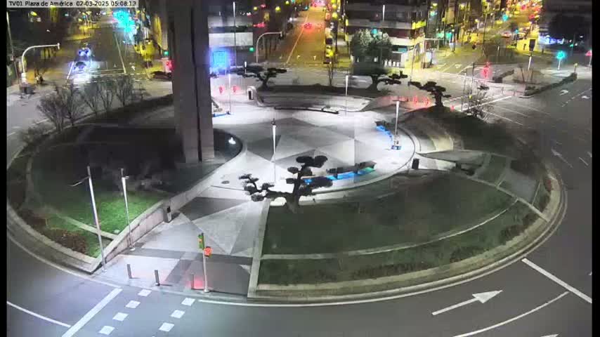 A nighttime view of a circular plaza with geometric landscaping, small trees, and a roadway circling it.
