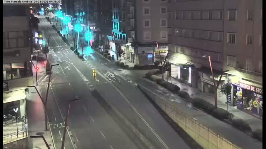 A mostly empty city street at night, lit by streetlights, shows several buildings and few cars.