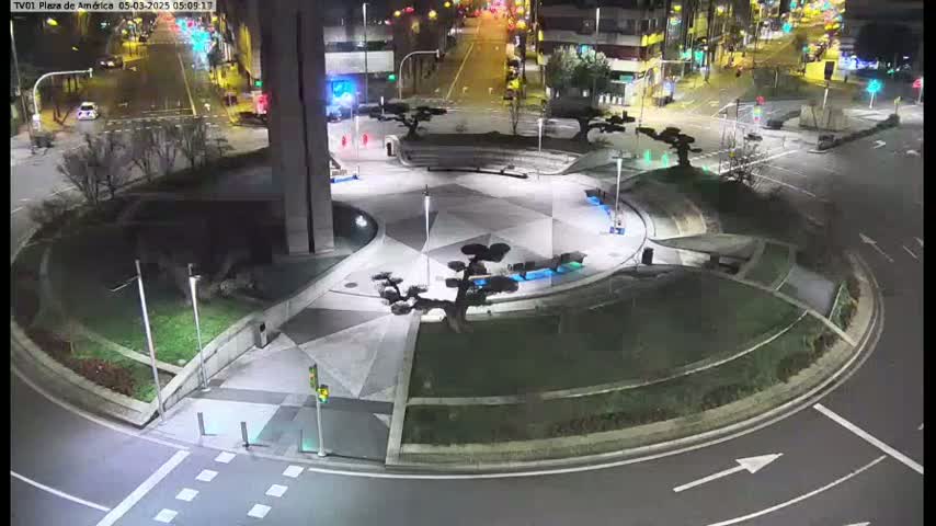 A nighttime aerial view shows a circular plaza with landscaping and a roadway surrounding it.