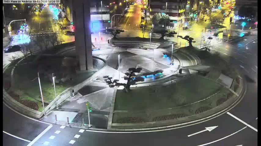 A nighttime aerial view shows a circular plaza with landscaping and a roadway circling it.
