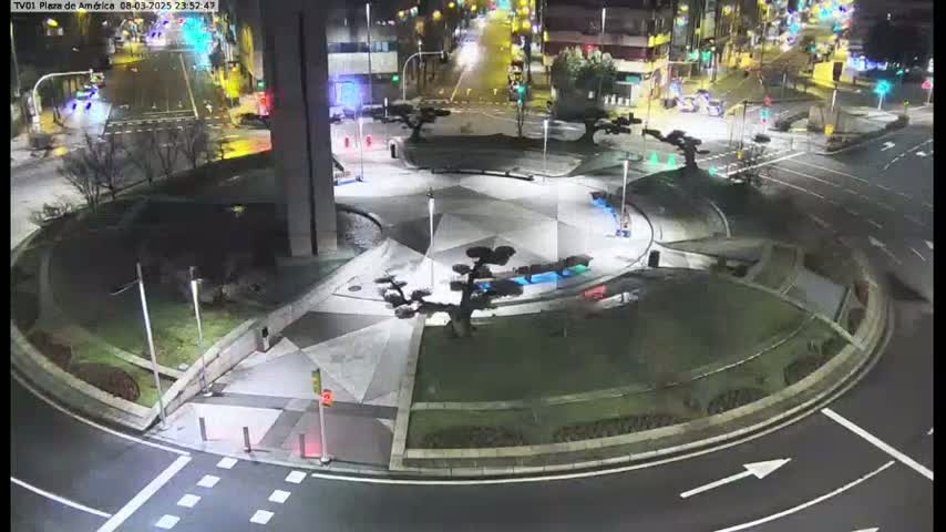 A nighttime aerial view of a roundabout with landscaped islands and artificial trees, surrounded by roadways with minimal traffic.