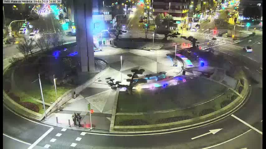 A nighttime aerial view of a roundabout with landscaped areas and several cars visible on the surrounding roads.