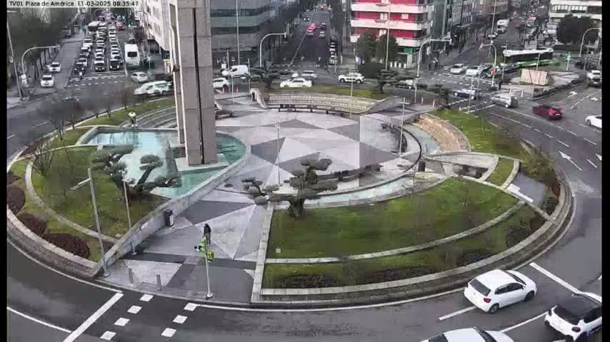 A landscaped roundabout with a geometric pattern in the center is surrounded by a road with several cars; it is overcast.