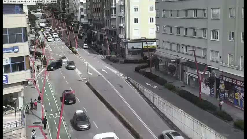 A street scene shows several cars driving on a multi-lane road that passes by buildings on a mostly cloudy day.