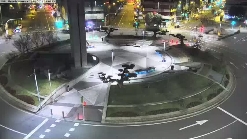 A nighttime aerial view of a circular plaza with landscaped areas and surrounding roads, illuminated by streetlights.