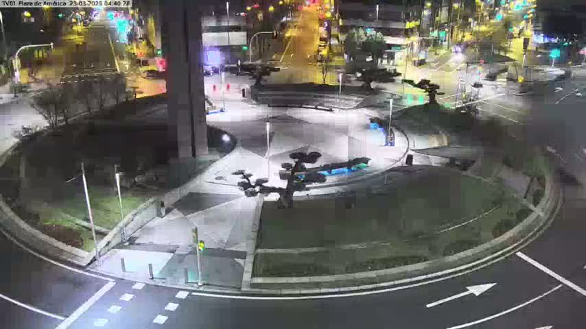 A nighttime aerial view of a roundabout in a city, with landscaped areas and streetlights illuminating the scene.