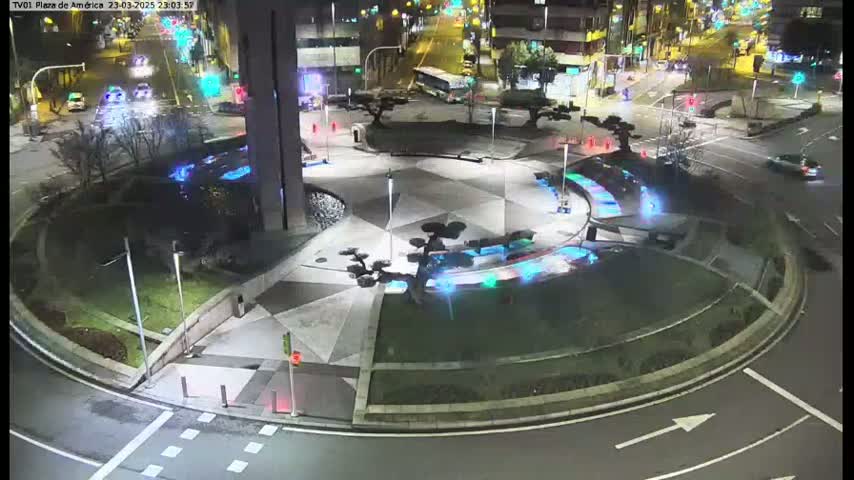 A nighttime aerial view of a roundabout with illuminated landscaping features and sparse traffic.