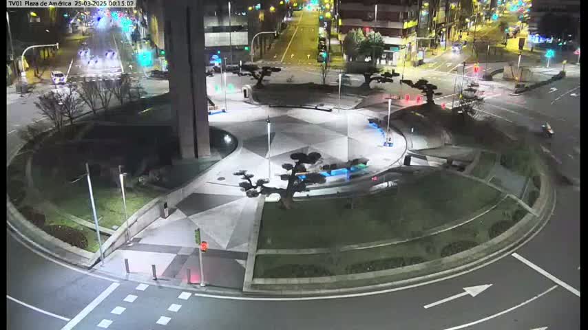 A nighttime view of a paved roundabout with landscaped areas and some traffic on surrounding roads.
