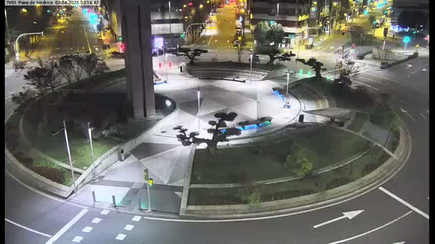 A nighttime aerial view of a circular plaza with landscaping and geometric pavement, surrounded by roads and buildings.