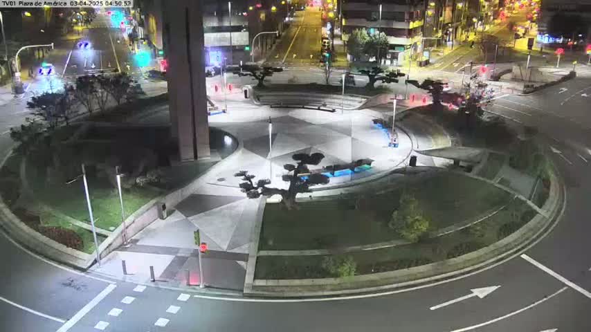 A nighttime aerial view of a circular plaza with geometric landscaping, trees, and surrounding roadways.
