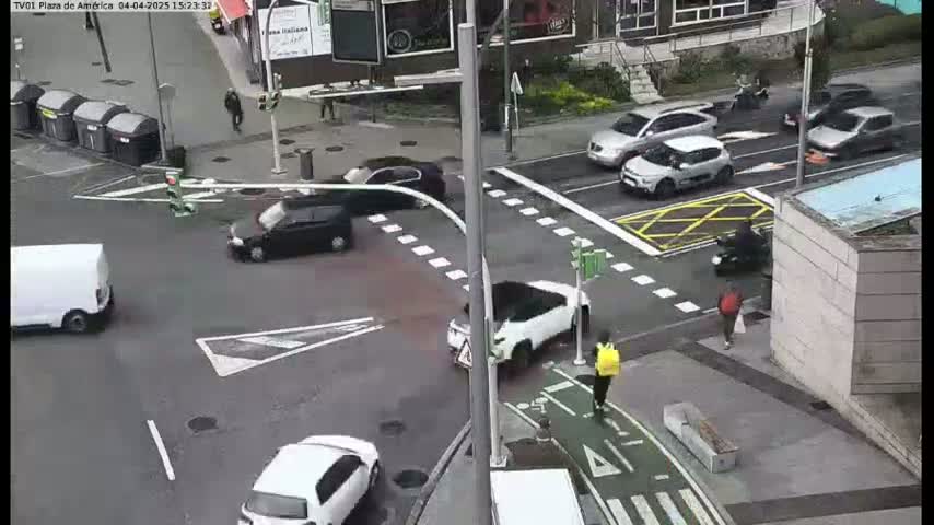 A busy city intersection with several cars and pedestrians, under an overcast sky.