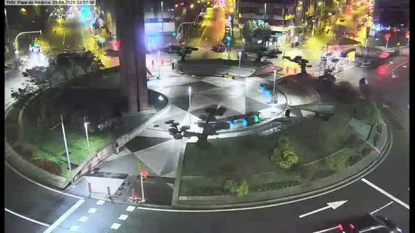A nighttime aerial view of a roundabout with landscaped areas and sparse vehicle traffic.