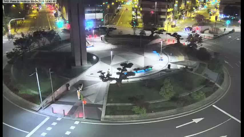 An elevated nighttime view shows a circular plaza with landscaping and walkways, surrounded by roads with minimal traffic.