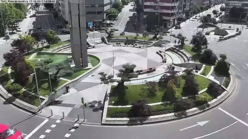 A sunny day reveals a circular plaza with landscaped gardens, a central paved area, and surrounding streets.