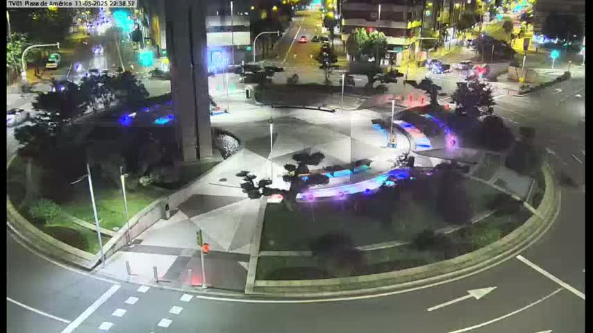 A nighttime aerial view of a circular plaza with geometric landscaping, illuminated by artificial lights, surrounded by roadways and buildings.