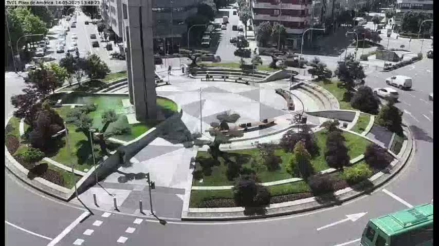 A landscaped traffic circle with a central plaza, surrounded by buildings and roadways on a sunny day.