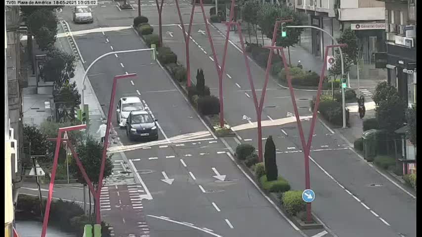 A mostly empty city street with two cars at an intersection, under an overcast sky.