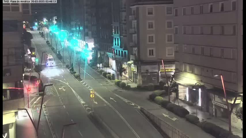 A mostly empty, nighttime street scene shows a few vehicles and some pedestrians under artificial street lights.