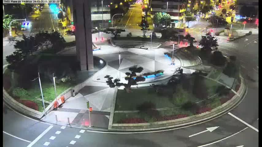 A nighttime aerial view of a circular plaza with geometric landscaping, bordered by roads and buildings.