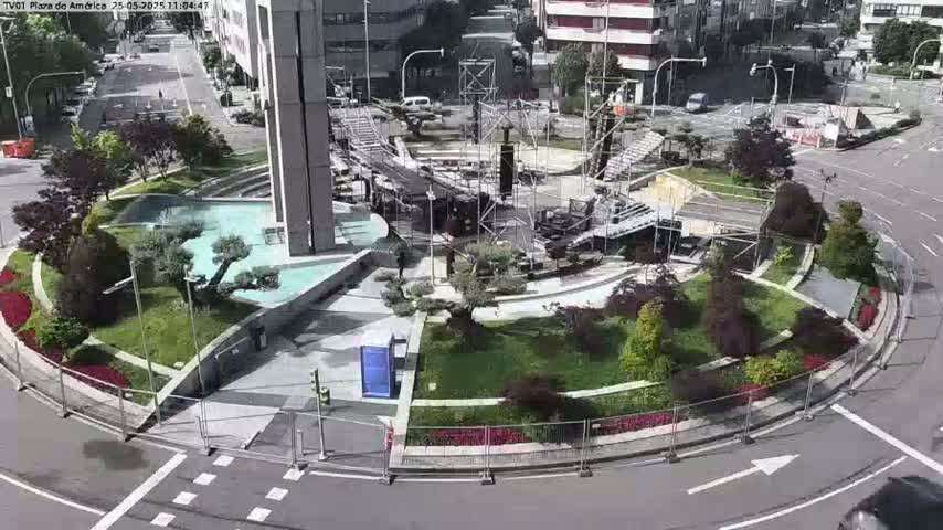 A high-angle view shows a circular plaza under construction, surrounded by landscaped areas and roadways on a sunny day.