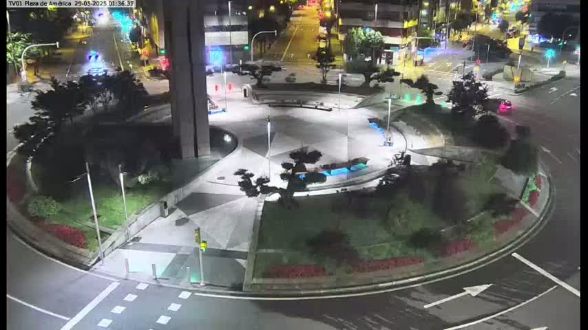 A nighttime aerial view of a roundabout with landscaped islands and several cars on the surrounding streets.