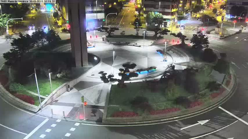 A nighttime aerial view of a circular plaza with landscaping and walkways, surrounded by roads with minimal traffic.