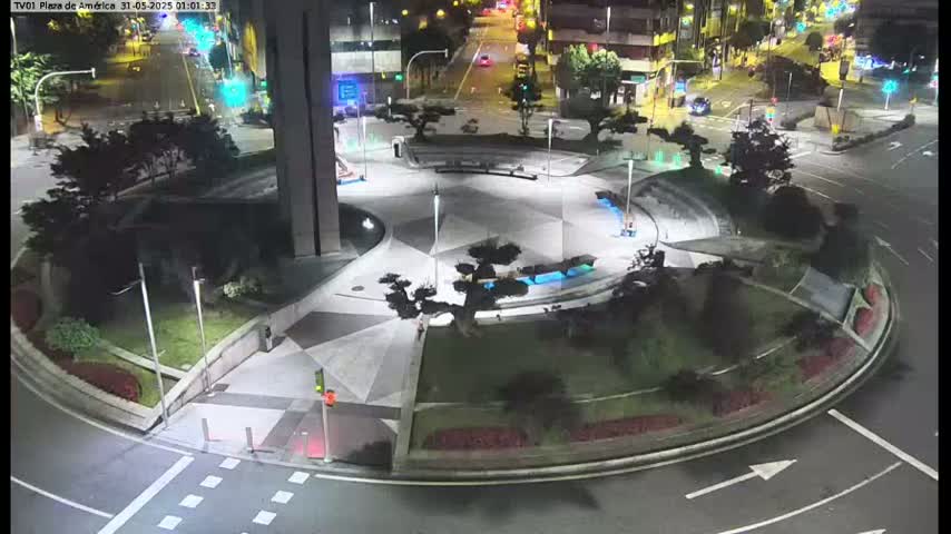 A nighttime aerial view shows a circular plaza with landscaped areas and low lighting, surrounded by roadways with minimal traffic.