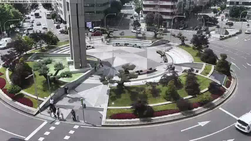 A landscaped traffic circle with a central plaza, surrounded by buildings and roadways, on a sunny day.