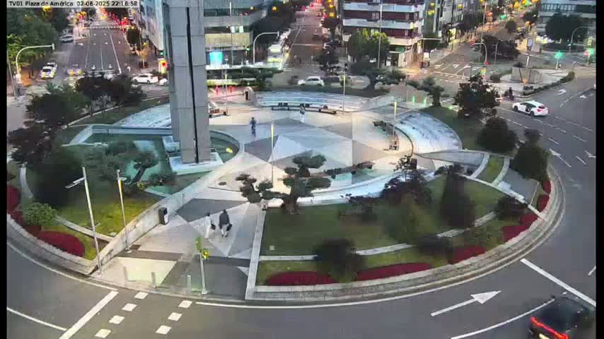 A circular plaza with geometric landscaping and a central water feature is surrounded by a roadway at dusk.